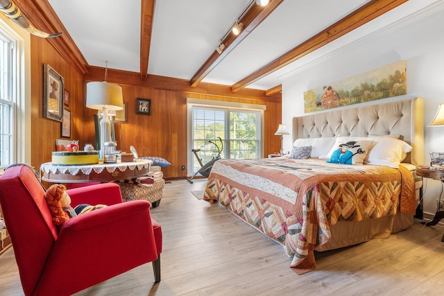 bedroom with track lighting, wood finished floors, wood walls, and beam ceiling
