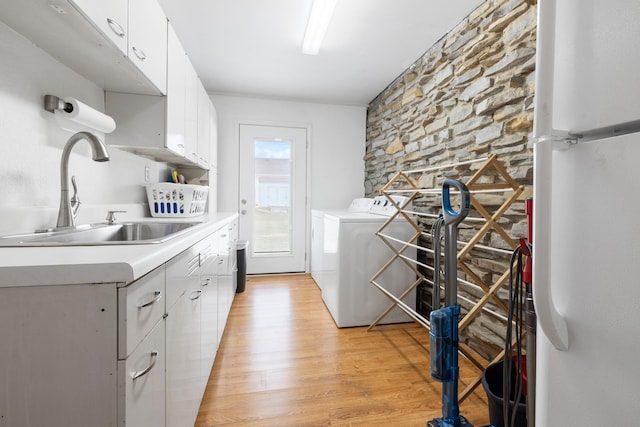 clothes washing area featuring a sink, washing machine and clothes dryer, cabinet space, and light wood-style flooring