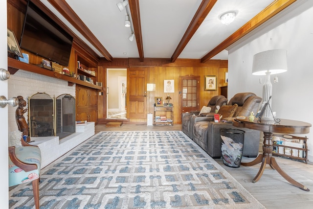 living room with wooden walls, a brick fireplace, beam ceiling, and wood finished floors