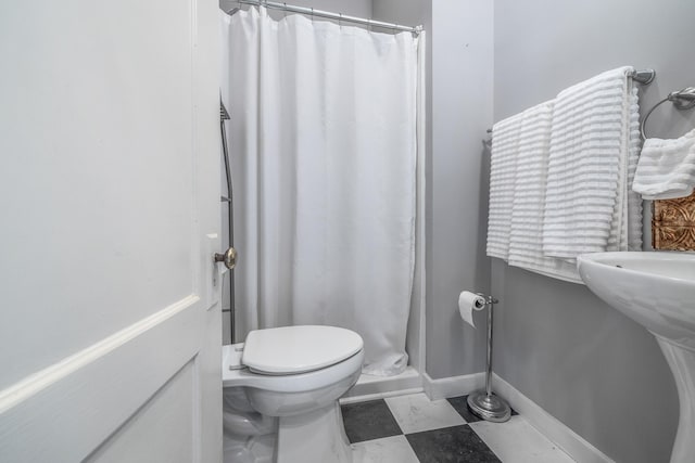 bathroom featuring toilet, a shower with shower curtain, and baseboards