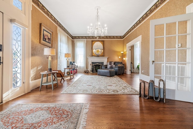 sitting room with baseboards, wallpapered walls, ornamental molding, a chandelier, and wood finished floors