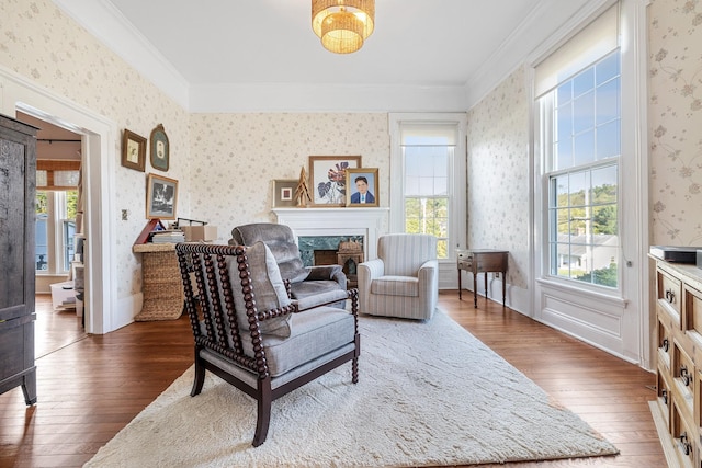 living area featuring crown molding, a premium fireplace, wallpapered walls, plenty of natural light, and hardwood / wood-style flooring