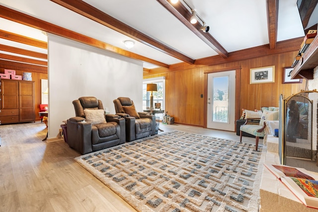 living area featuring light wood finished floors, wood walls, beamed ceiling, and rail lighting
