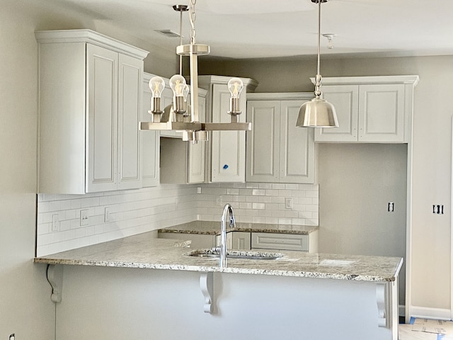 kitchen featuring light stone counters, pendant lighting, backsplash, white cabinetry, and a breakfast bar