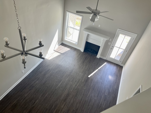 unfurnished living room with ceiling fan with notable chandelier, a high ceiling, dark wood-type flooring, and a wealth of natural light