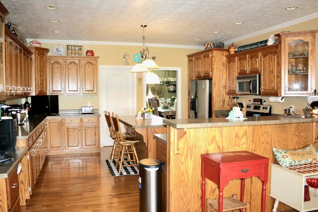 kitchen with appliances with stainless steel finishes, wood-type flooring, crown molding, and a breakfast bar area