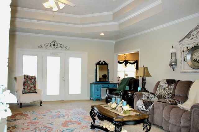 carpeted living room with a raised ceiling, ornamental molding, ceiling fan, and french doors