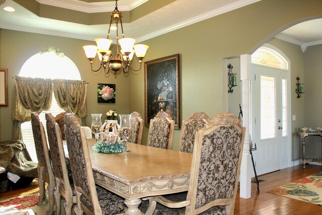 dining room with wood-type flooring, ornamental molding, a tray ceiling, and a notable chandelier