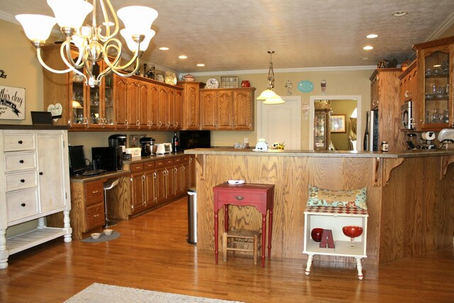 kitchen with hardwood / wood-style flooring, kitchen peninsula, crown molding, an inviting chandelier, and decorative light fixtures