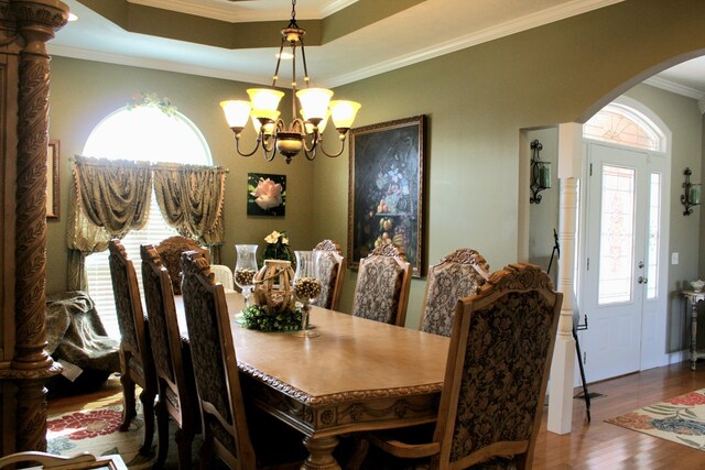 dining room with wood-type flooring, a tray ceiling, crown molding, and a chandelier