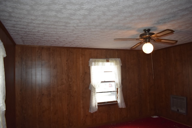 empty room featuring ceiling fan, heating unit, wooden walls, and a textured ceiling