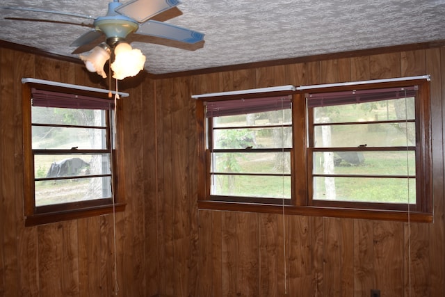 unfurnished room with ceiling fan, a textured ceiling, wood walls, and ornamental molding