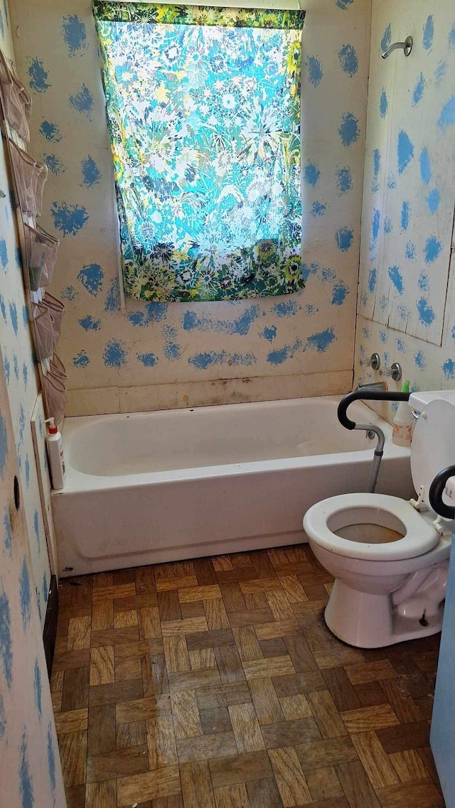 bathroom with parquet floors, a tub, and toilet