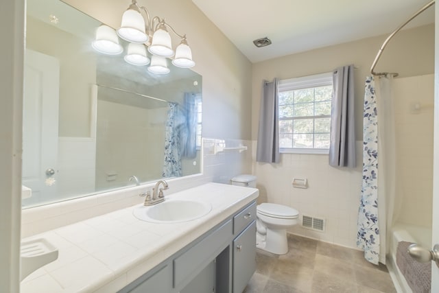 full bathroom featuring shower / bath combination with curtain, tile walls, an inviting chandelier, vanity, and toilet