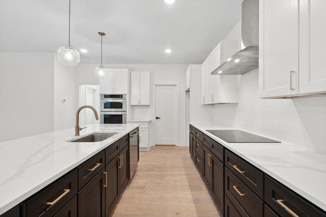 kitchen featuring sink, wall chimney exhaust hood, decorative light fixtures, white cabinets, and appliances with stainless steel finishes