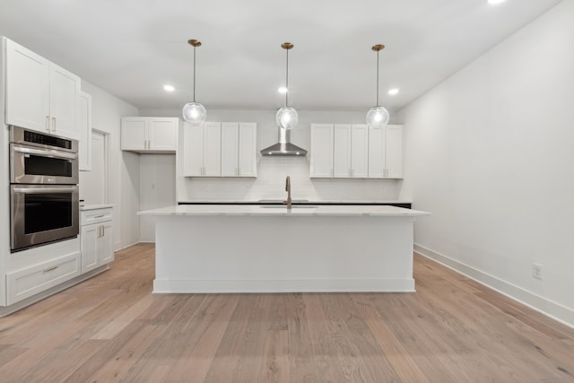 kitchen with white cabinets, stainless steel double oven, a kitchen island with sink, and hanging light fixtures