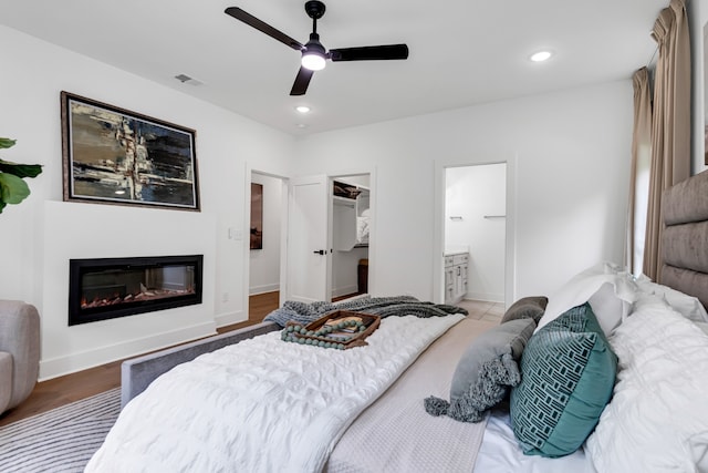 bedroom featuring ensuite bathroom, a walk in closet, hardwood / wood-style flooring, ceiling fan, and a closet