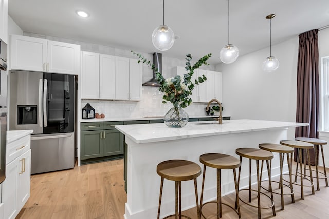 kitchen featuring sink, hanging light fixtures, stainless steel fridge with ice dispenser, a kitchen island with sink, and light wood-type flooring