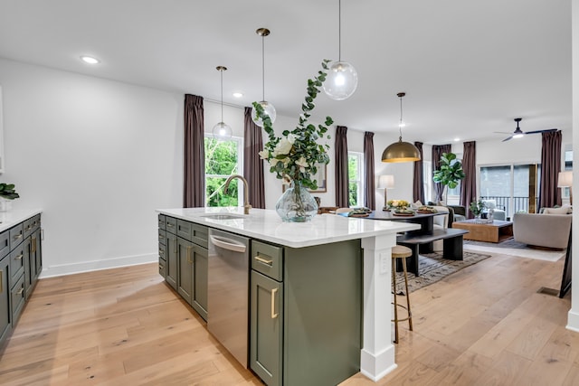 kitchen featuring sink, light hardwood / wood-style flooring, stainless steel dishwasher, an island with sink, and decorative light fixtures