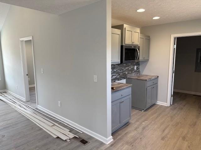 kitchen with a textured ceiling, gray cabinets, light hardwood / wood-style flooring, and tasteful backsplash