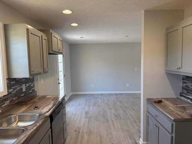 kitchen featuring decorative backsplash, stainless steel dishwasher, gray cabinetry, sink, and light hardwood / wood-style flooring