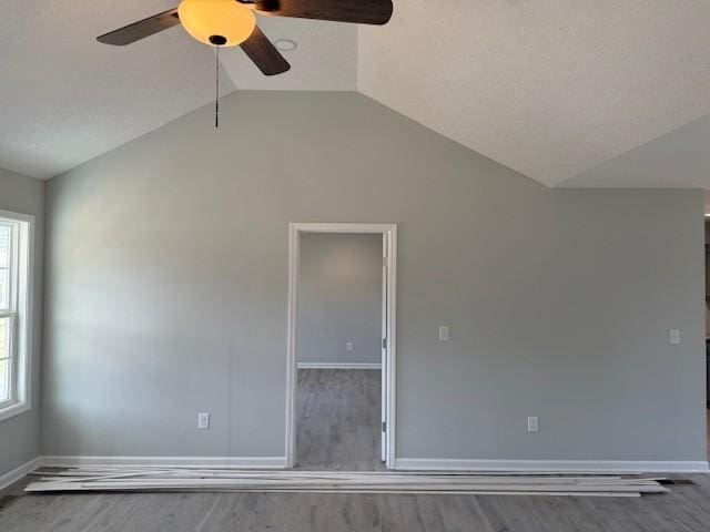 empty room featuring ceiling fan, wood-type flooring, a wealth of natural light, and vaulted ceiling