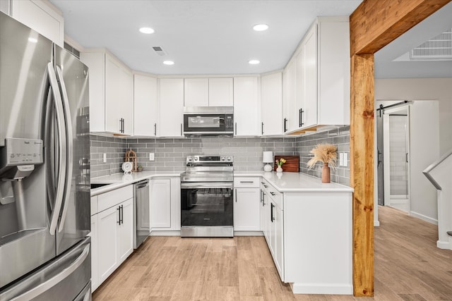 kitchen featuring white cabinetry, a barn door, light hardwood / wood-style flooring, stainless steel appliances, and decorative backsplash