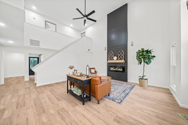 living room featuring ceiling fan, a fireplace, light wood-type flooring, and a high ceiling