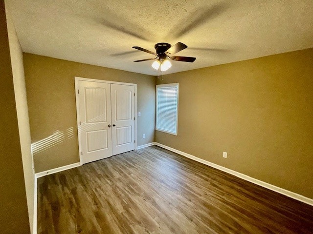 unfurnished bedroom with ceiling fan, a closet, dark wood-type flooring, and a textured ceiling