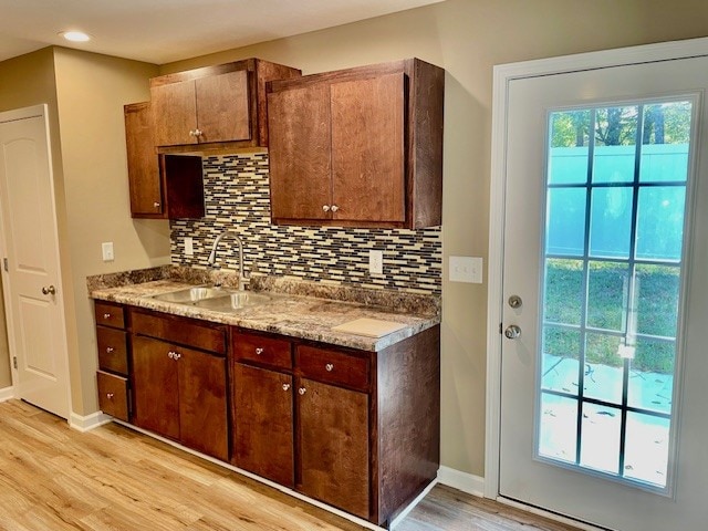 kitchen with backsplash, light stone countertops, light wood-type flooring, and sink