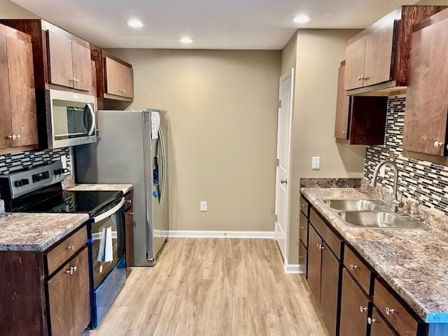 kitchen featuring appliances with stainless steel finishes, baseboards, decorative backsplash, light wood finished floors, and a sink