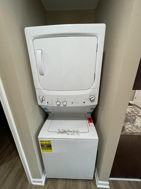 laundry area featuring laundry area, baseboards, stacked washer / dryer, and wood finished floors