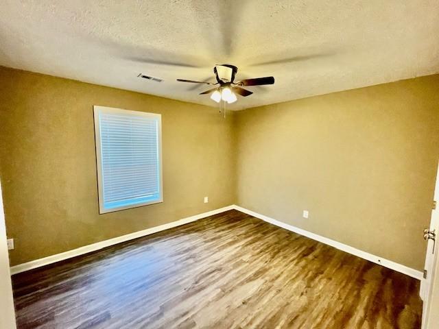 spare room featuring a textured ceiling, wood finished floors, ceiling fan, and baseboards
