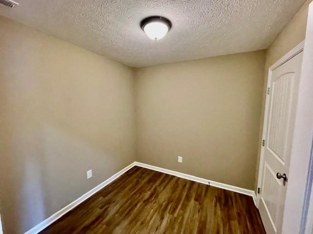spare room with visible vents, baseboards, a textured ceiling, and dark wood-style floors