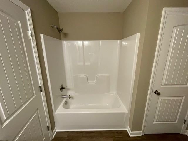 bathroom featuring wood finished floors, tub / shower combination, and baseboards