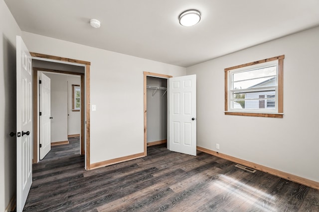 unfurnished bedroom with dark hardwood / wood-style flooring, multiple windows, and a closet