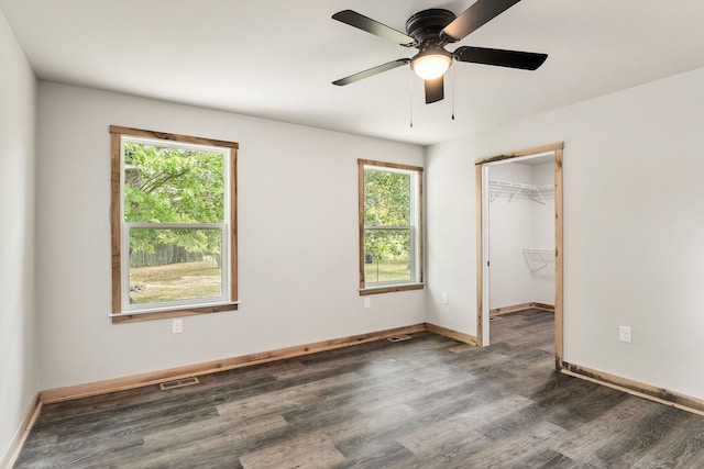 unfurnished bedroom with dark hardwood / wood-style flooring, a walk in closet, multiple windows, and ceiling fan