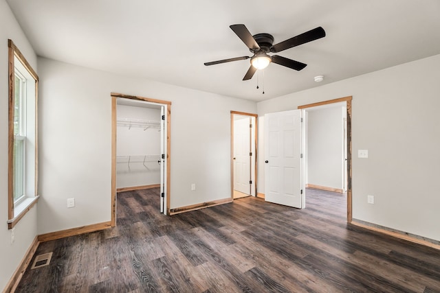 unfurnished bedroom with dark wood-type flooring, ceiling fan, a closet, and a walk in closet