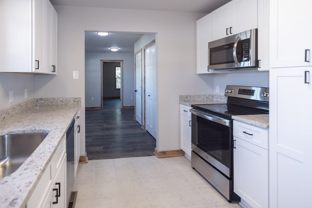 kitchen featuring white cabinets, light wood-type flooring, appliances with stainless steel finishes, and light stone countertops