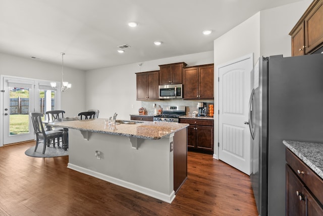 kitchen with dark hardwood / wood-style floors, an island with sink, a kitchen breakfast bar, an inviting chandelier, and appliances with stainless steel finishes