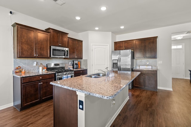 kitchen with light stone counters, dark wood-type flooring, sink, an island with sink, and stainless steel appliances