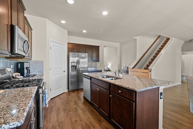 kitchen with light stone counters, sink, a center island with sink, appliances with stainless steel finishes, and hardwood / wood-style floors