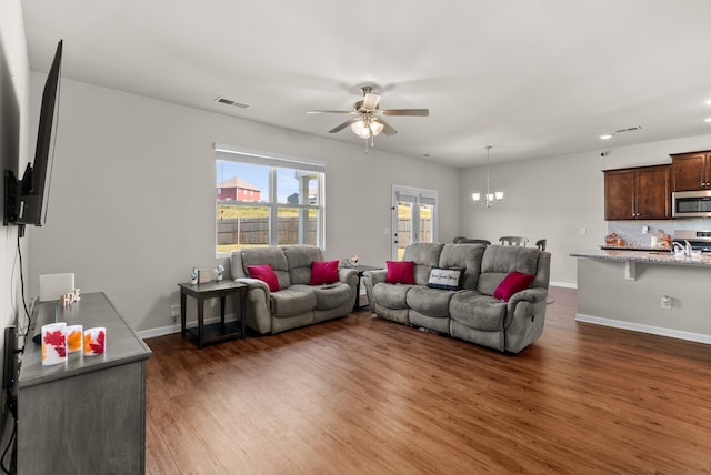 living room featuring ceiling fan with notable chandelier and dark wood-type flooring