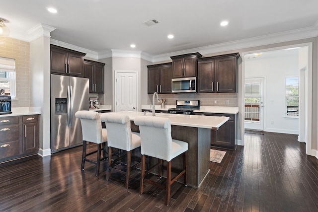 kitchen with an island with sink, appliances with stainless steel finishes, plenty of natural light, and dark hardwood / wood-style flooring