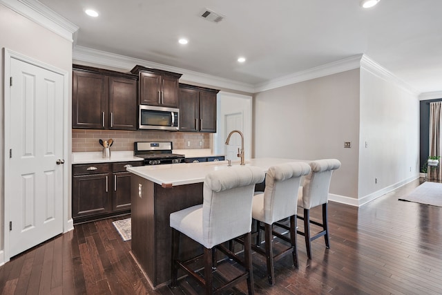 kitchen featuring dark brown cabinets, a center island with sink, appliances with stainless steel finishes, dark hardwood / wood-style flooring, and decorative backsplash