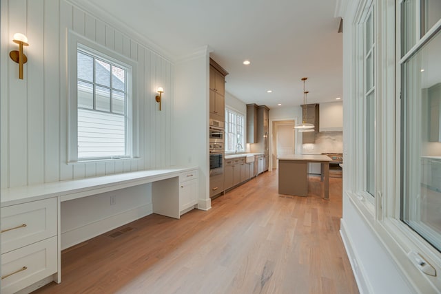 kitchen featuring decorative backsplash, built in desk, hanging light fixtures, crown molding, and light hardwood / wood-style floors