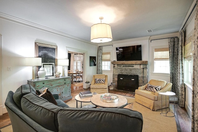 living room with crown molding, hardwood / wood-style flooring, and a stone fireplace