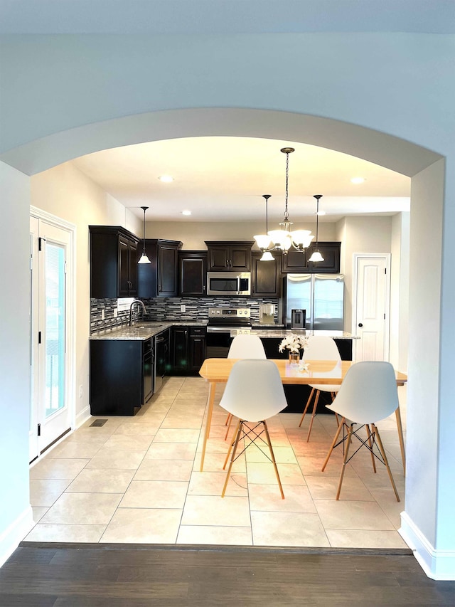 kitchen with stainless steel appliances, hanging light fixtures, decorative backsplash, and a wealth of natural light