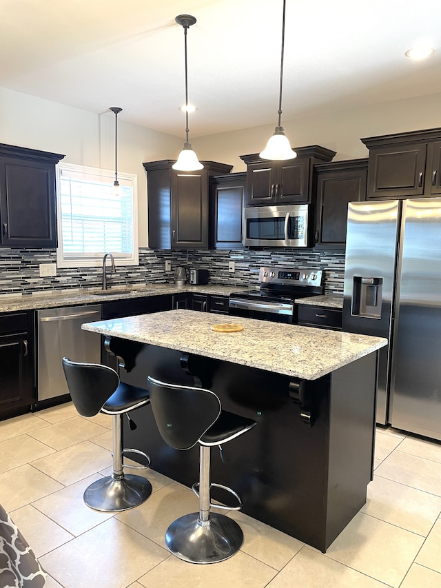 kitchen featuring pendant lighting, a kitchen bar, a kitchen island, decorative backsplash, and stainless steel appliances