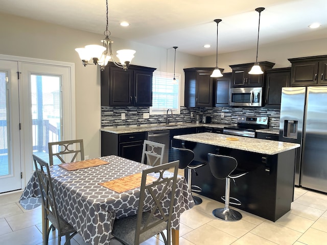 kitchen with appliances with stainless steel finishes, hanging light fixtures, a kitchen island, and a wealth of natural light